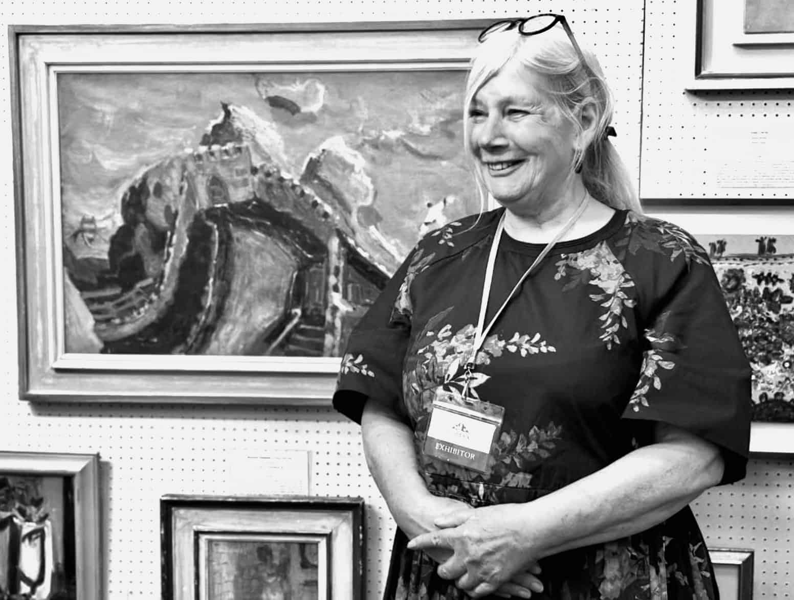 Smiling female exhibitor standing before landscape paintings at art show